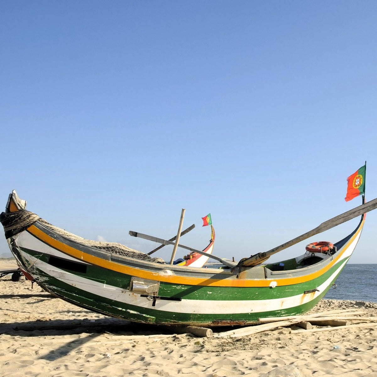 Traditional Portuguese fishing boats on a sandy beach, flying Portuguese flags beside the Atlantic Ocean.