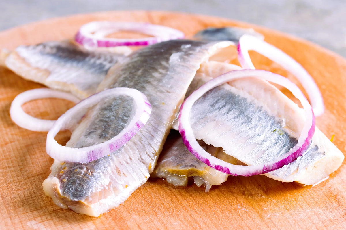In Scheiben geschnittene Heringsfilets mit roten Zwiebelringen auf einem Holzbrett – ein klassisches schwedisches Heringsgericht
